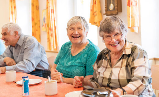 Zwei Seniorinnen und ein Senior sitzen gemeinsam am Kaffeetisch