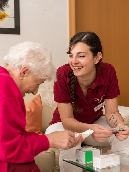 Seniorin bekommt von Pflegerin Hilfe beim Tabletten sortieren 