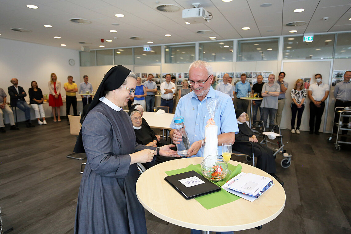 Stiftungsarchivar Ewald Graf verabschiedet sich nach 23 Jahren in den Ruhestand. Die Generalvikarin Sr. M. Dorothea überreicht zum Dank heilendes Wasser aus der Kloster Quelle in Heiligenbronn.