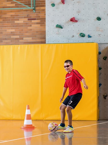 Junge mit Sehbehinderung spielt in Schulsporthalle für Kinder mit Sinnesbehinderung