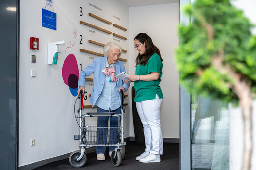 Pflegeperson und ältere Dame unterhalten sich im Flur stehend