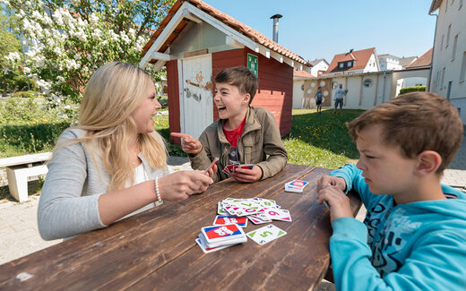 Zwei Kinder sitzen mit Betreuerin zusammen und spielen ein Spiel 