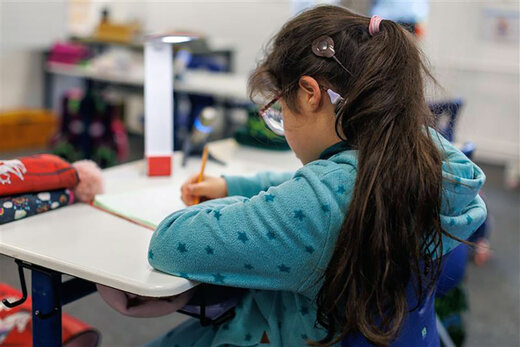 Jugendliche mit CI-Implantat sitzt an einem Schultisch und schreibt etwas ins Heft