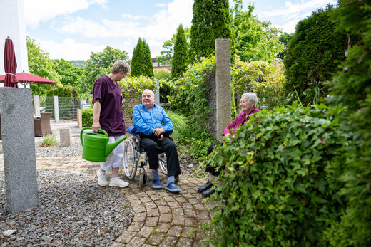 Zwei ältere Menschen im Rollstuhl sitzen unterhalten sich mit Pflegeperson im Garten des Altenzentrums St. Josef