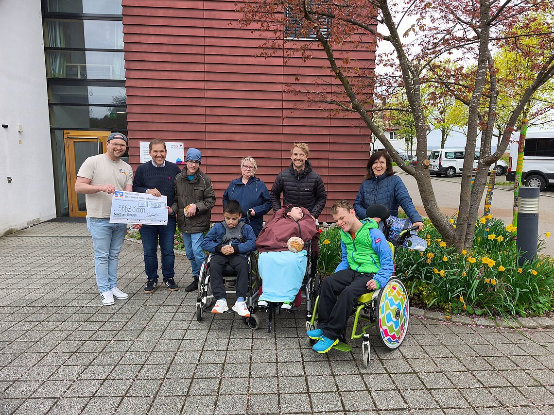 Bäckermeister Valentin Schmidt (links) übergibt 500 Euro aus seiner Brot-Spendenaktion an Dr. Marcus Adrian (2. v. l.), Kinder und Mitarbeitende des SBBZ Sehen in Baindt. _credit: Stefanie Keppeler