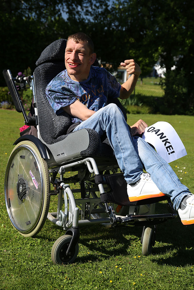 Junger Mann mit Behinderung im Rollstuhl hält ein "Danke"-Schild in der Hand