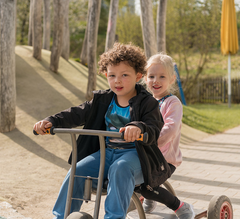 Junge und Mädchen fahren gemeinsam auf einem Dreirad