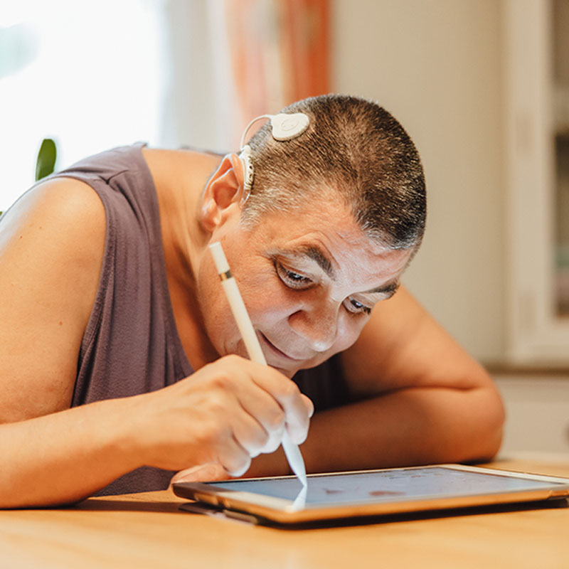 Frau mit Sehbehinderung und Cochlear Implantat schreibt auf einem Tablet