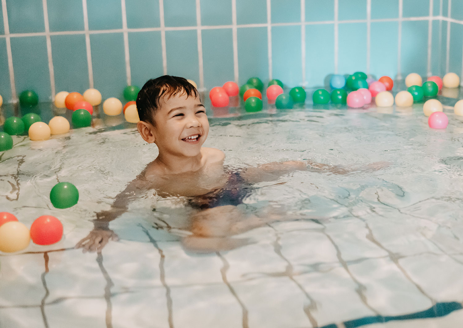 Ein Junge im Wasser des Therapiebades mit bunten Kunststoffbällen