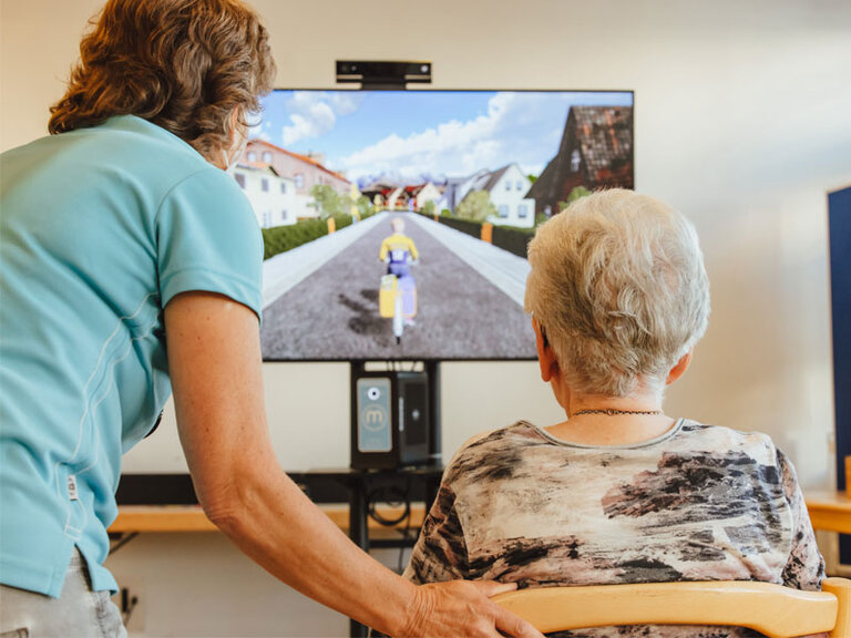 ältere Frau und Betreuerin an einer Spielkonsole vor dem Fernseher