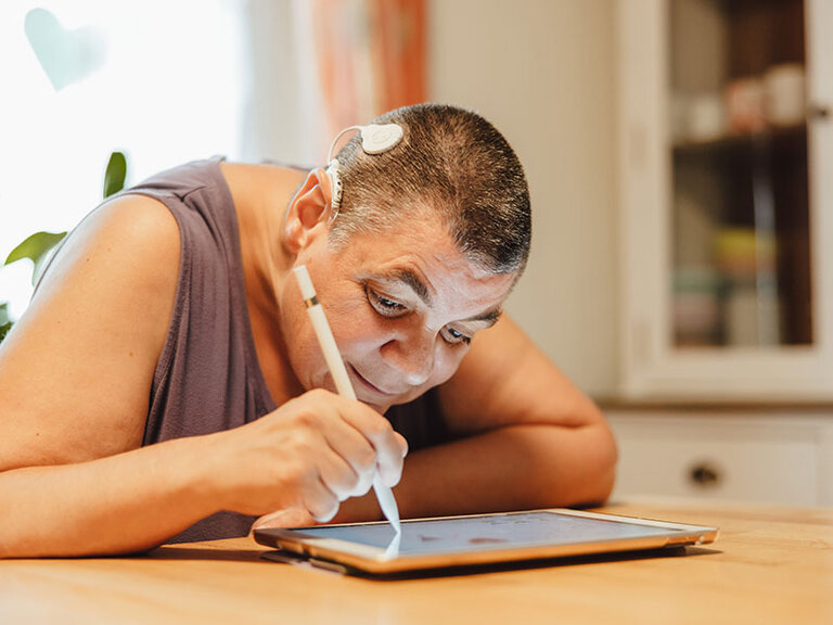Frau mit Sehbehinderung und Cochlear Implantat schreibt auf einem Tablet