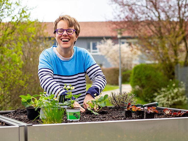 Junge Frau mit Behinderung lachend am Hochbeet Pflanzen einsetzend
