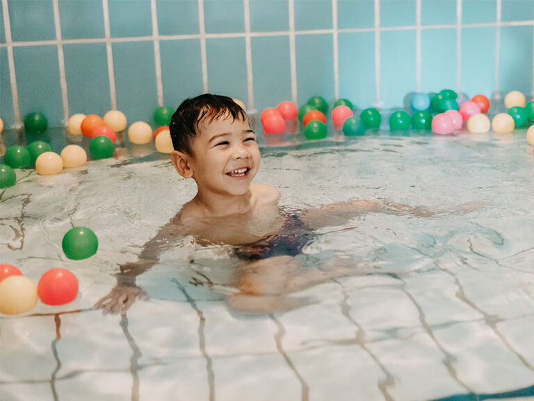 Ein Junge im Therapiebad mit bunten Kunsstoffbällen