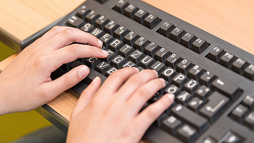 Finger eines Schülers auf einer PC-Tastatur für Menschen mit Sehbehinderung mit übergroßen Zeichen